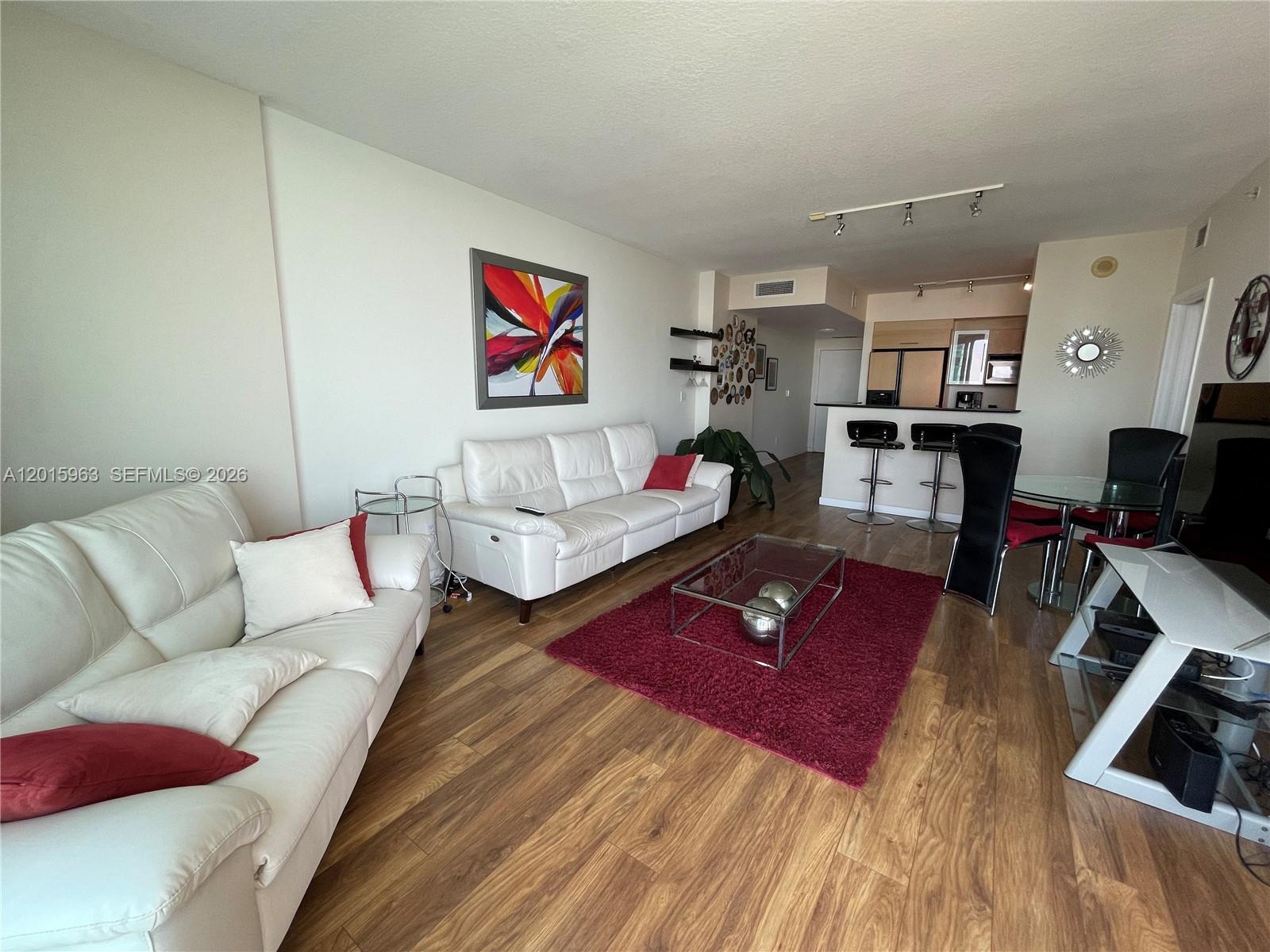A living room features white leather sofas, a red area rug, and an open kitchen — 335 S Biscayne Blvd # 3603, Miami FL 33131, MIAMI, FL