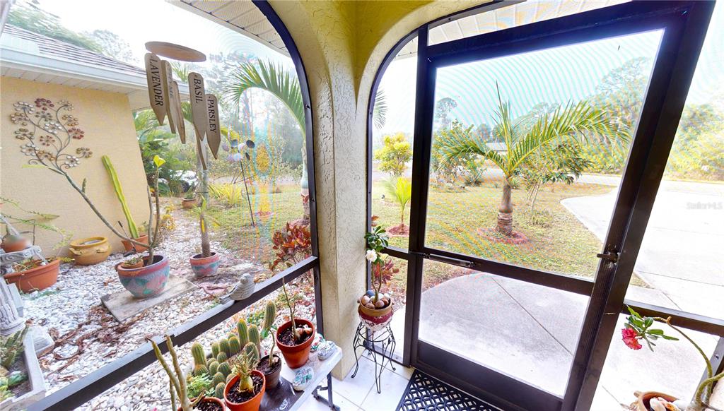 A screened-in porch features numerous potted plants, a hanging herb sign, and a screen door — 4114 COLLINGSWOOD BOULEVARD, PORT CHARLOTTE, FL