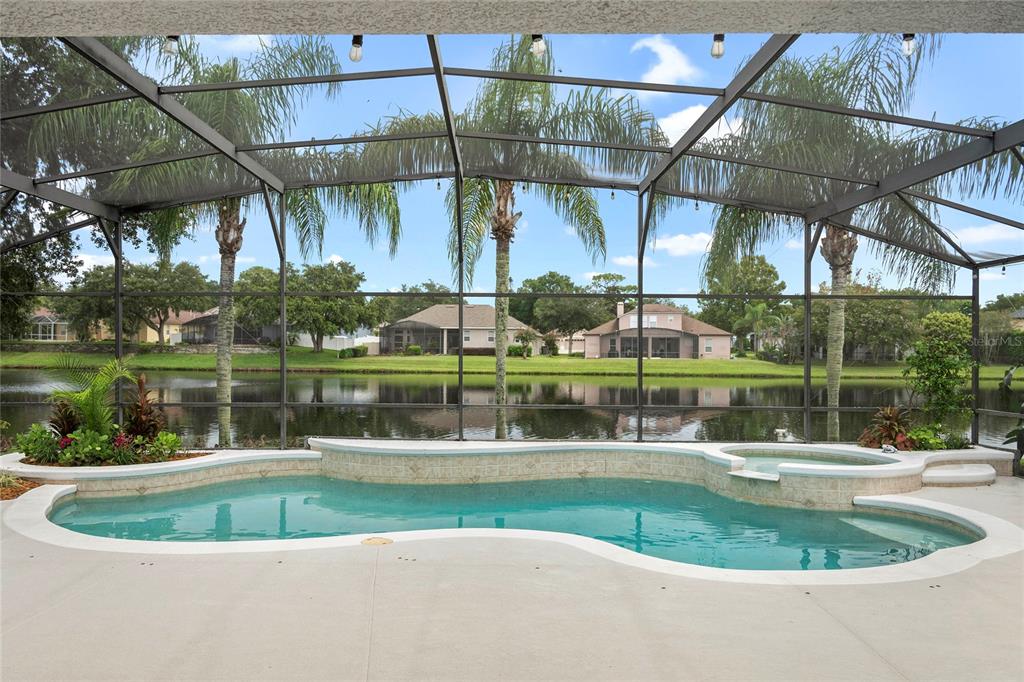 A screened-in pool and spa overlook a lake with houses in the background — 2848 ALOMA LAKE RUN, OVIEDO, FL