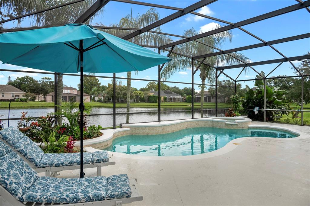 A screened-in pool patio features lounge chairs, a turquoise umbrella, and a view of water — 2848 ALOMA LAKE RUN, OVIEDO, FL