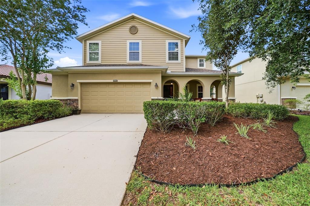 A two-story suburban house with a tan exterior, a two-car garage, and a landscaped yard — 24115 SAN GIOVANNI DRIVE, LAND O LAKES, FL