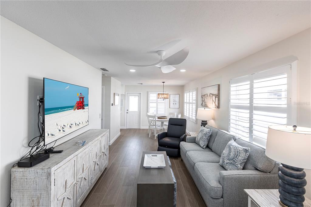 A living room features a gray sofa, a media console, and a dining area beyond — 6020 MIDNIGHT PASS ROAD UNIT 29, SARASOTA, FL