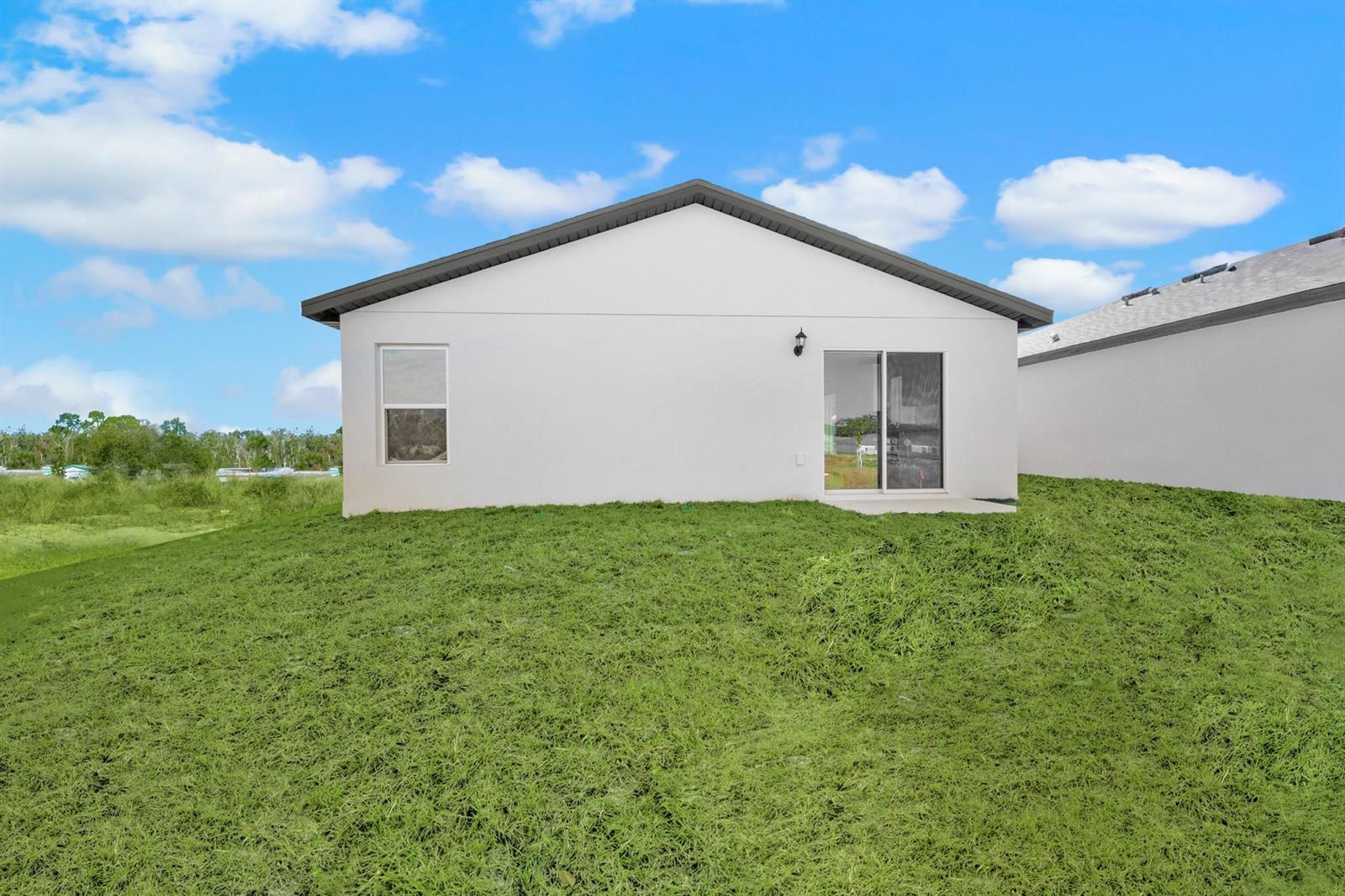 The exterior rear view of a white house features a sliding glass door and window — 8436 100th Court, Vero Beach FL 32967, VERO BEACH, FL