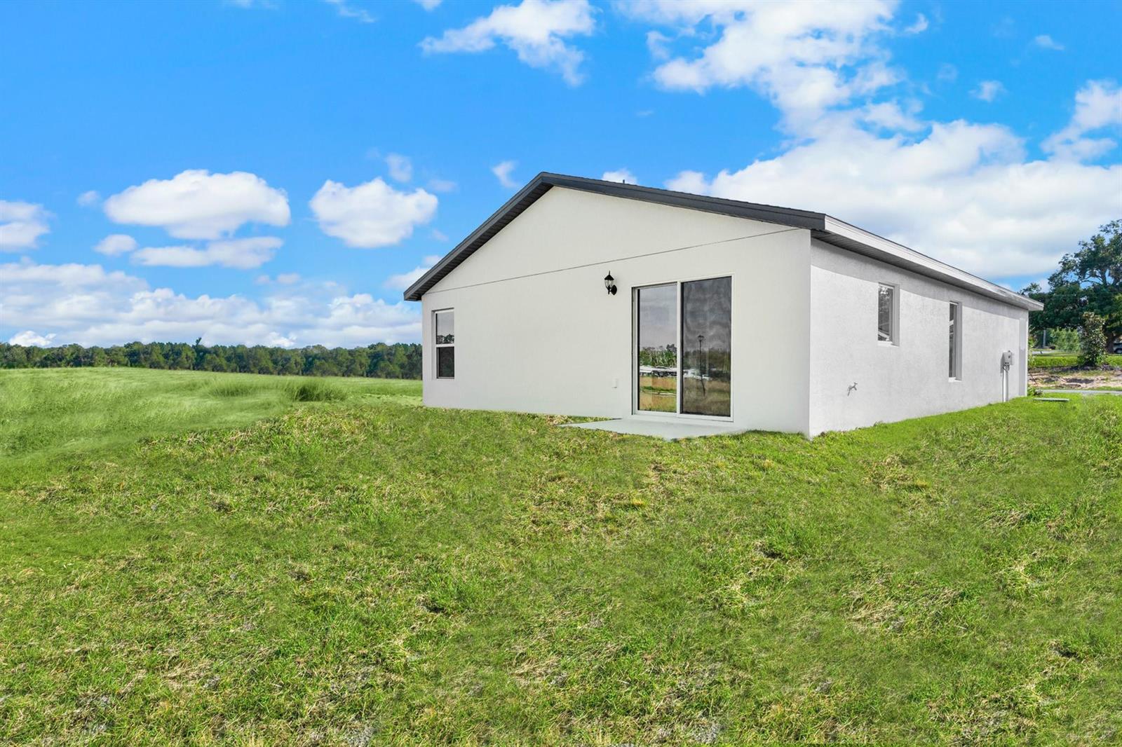 The exterior of a white, single-story house features a sliding glass door and grassy yard — 8436 100th Court, Vero Beach FL 32967, VERO BEACH, FL