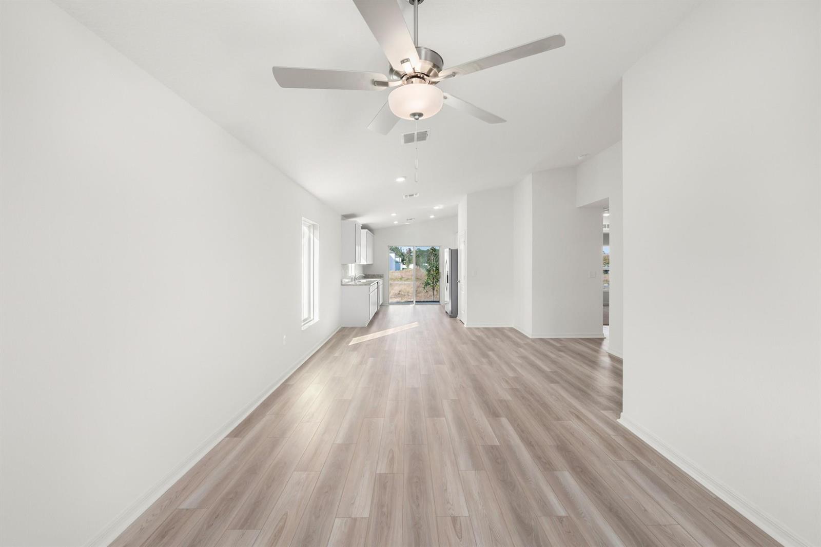 A long, open-concept living area with white walls, light wood flooring, and a ceiling fan — 8436 100th Court, Vero Beach FL 32967, VERO BEACH, FL