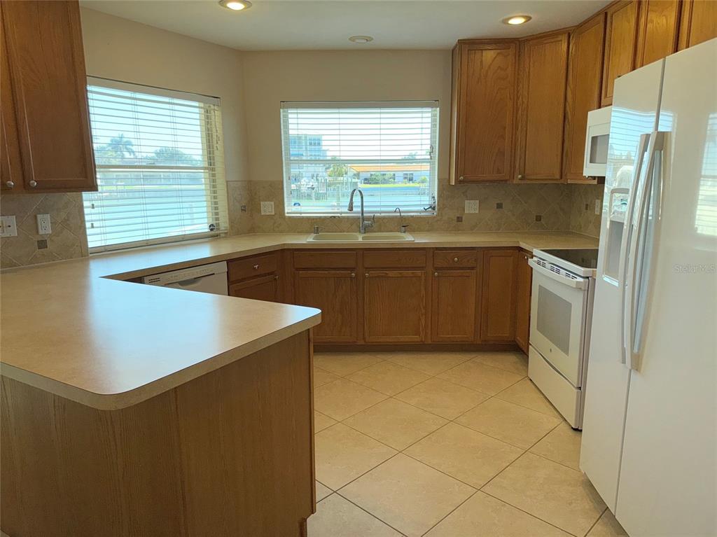 A kitchen with wood cabinets, white appliances, tile flooring, and a view of water — 228 HOWARD DRIVE, BELLEAIR BEACH, FL