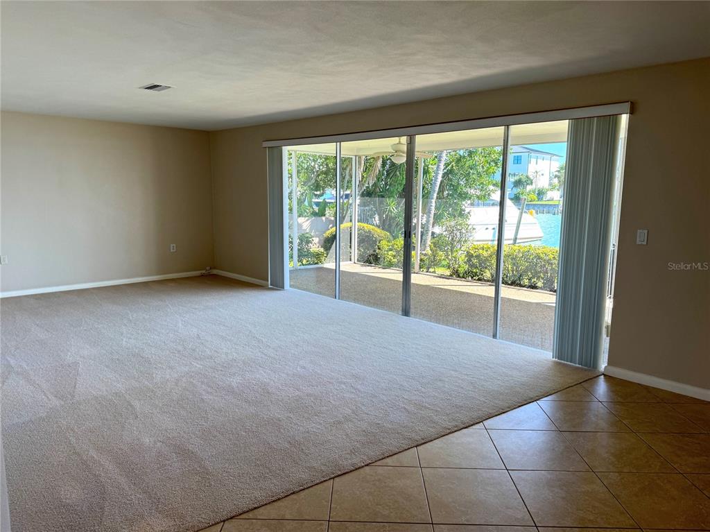 A living room with beige carpet, tile flooring, and large sliding glass doors overlooking water — 228 HOWARD DRIVE, BELLEAIR BEACH, FL