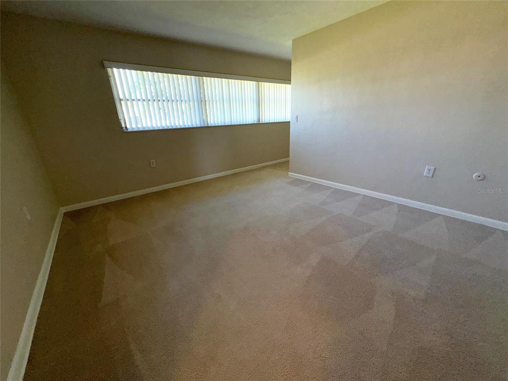 An empty bedroom features beige carpet, light-colored walls, and a long horizontal window with blinds — 228 HOWARD DRIVE, BELLEAIR BEACH, FL