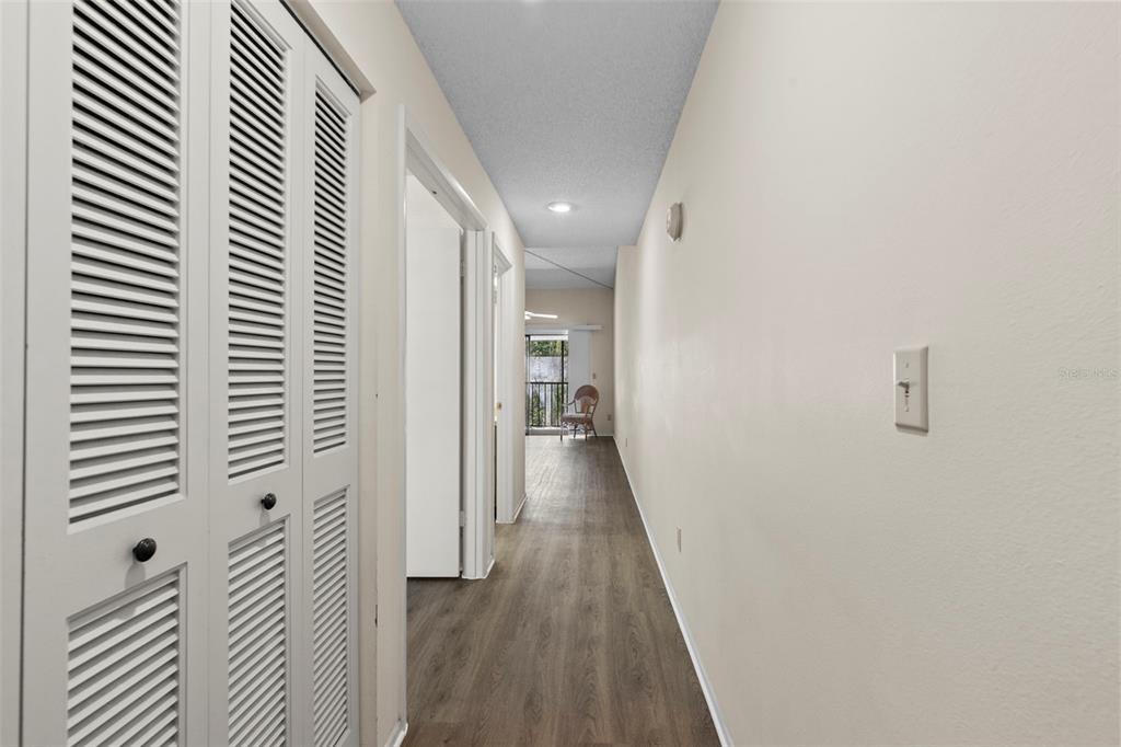 A hallway with light-colored walls, wood-look flooring, and white louvered closet doors on the left — 7832 NIAGARA AVENUE UNIT 323, TAMPA, FL