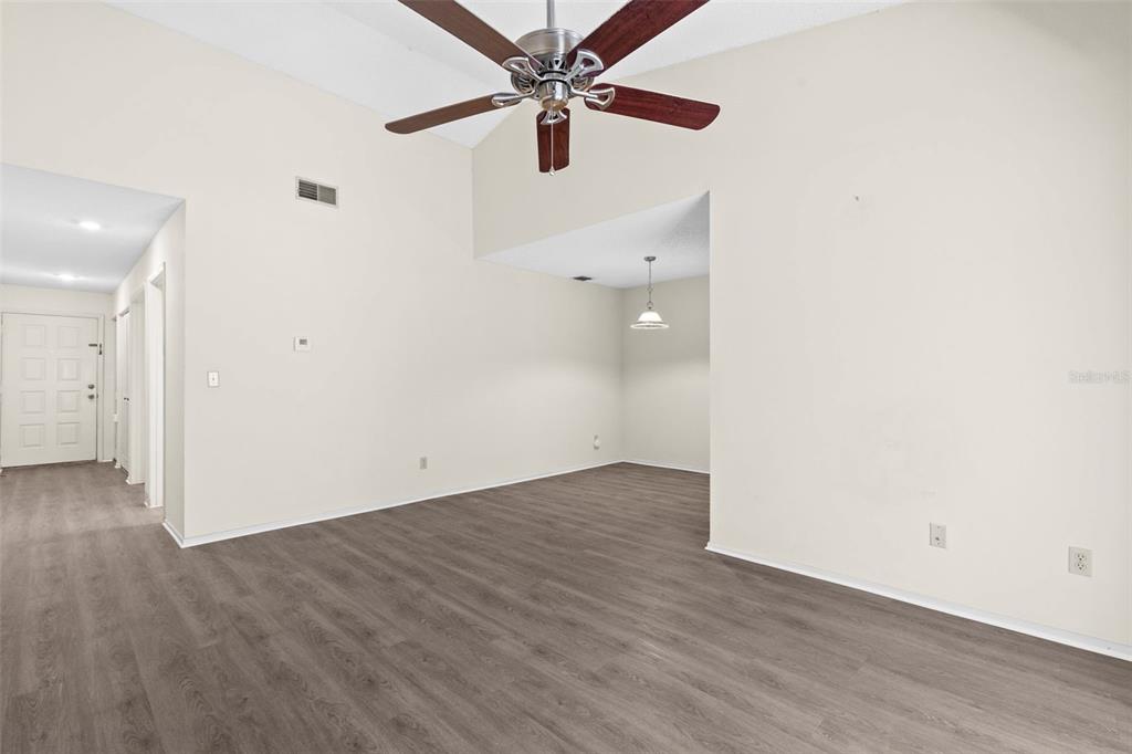 An empty living room with vaulted ceilings, a ceiling fan, and wood-look laminate flooring — 7832 NIAGARA AVENUE UNIT 323, TAMPA, FL