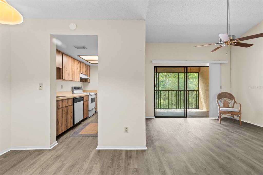 A living area with wood-look flooring leads to a kitchen and a screened-in balcony — 7832 NIAGARA AVENUE UNIT 323, TAMPA, FL