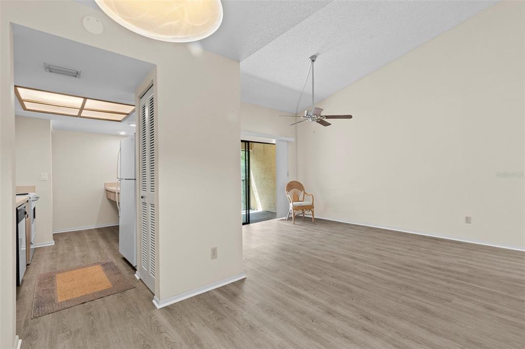 An open-concept living area with light wood-look flooring, a ceiling fan, and an adjacent kitchen — 7832 NIAGARA AVENUE UNIT 323, TAMPA, FL