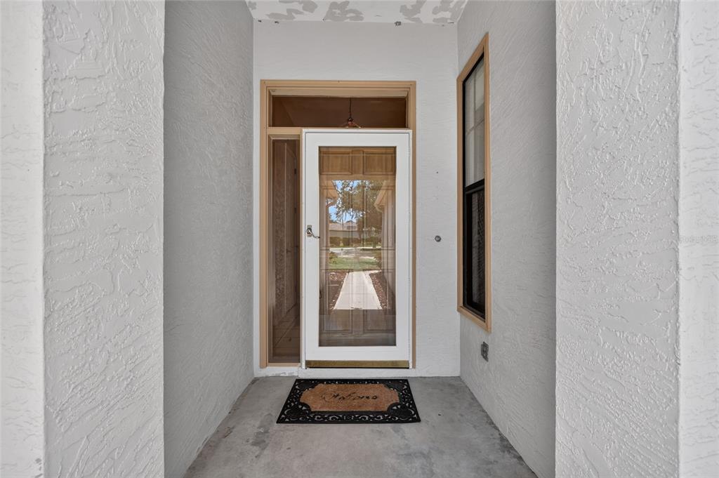 A white front door with a glass storm door sits within a covered entryway — 4588 NE 4TH STREET, OCALA, FL