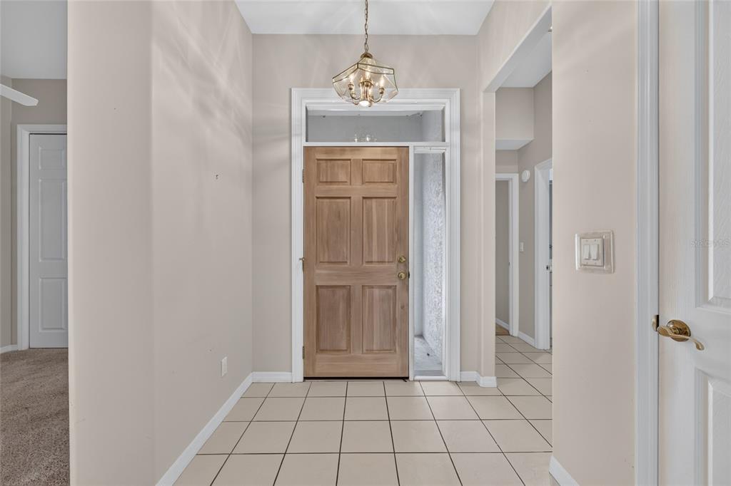 An entryway features a light-colored tile floor, a wooden front door, and a hanging chandelier — 4588 NE 4TH STREET, OCALA, FL
