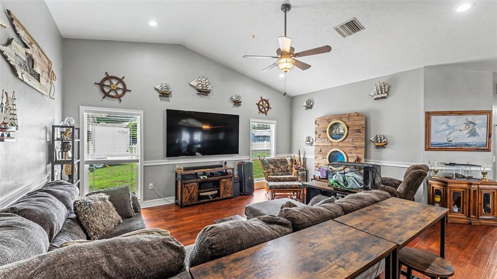 A living room features nautical decor, a large television, hardwood floors, and a vaulted ceiling — 36225 OAK KNOLL LOOP, DADE CITY, FL