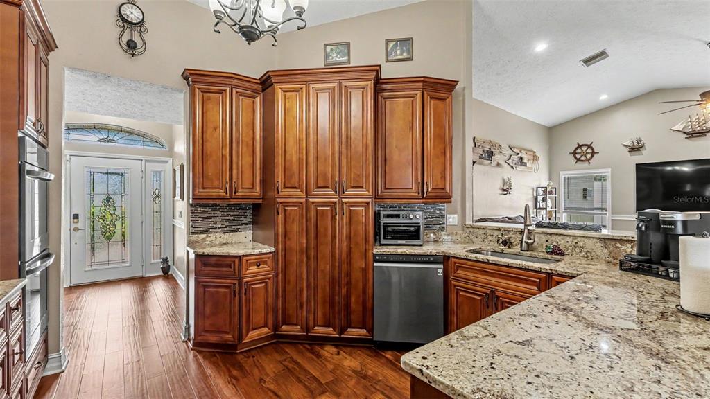 A kitchen features dark wood cabinets, granite countertops, stainless steel appliances, and hardwood flooring — 36225 OAK KNOLL LOOP, DADE CITY, FL