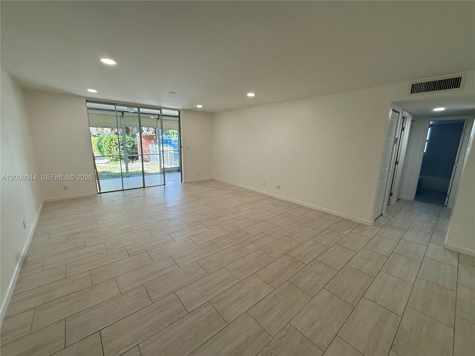 An empty room features light-colored tile flooring, white walls, recessed lighting, and sliding glass doors — 609 NE 14th Ave # 108, Hallandale Beach FL 33009, HALLANDALE BEACH, FL