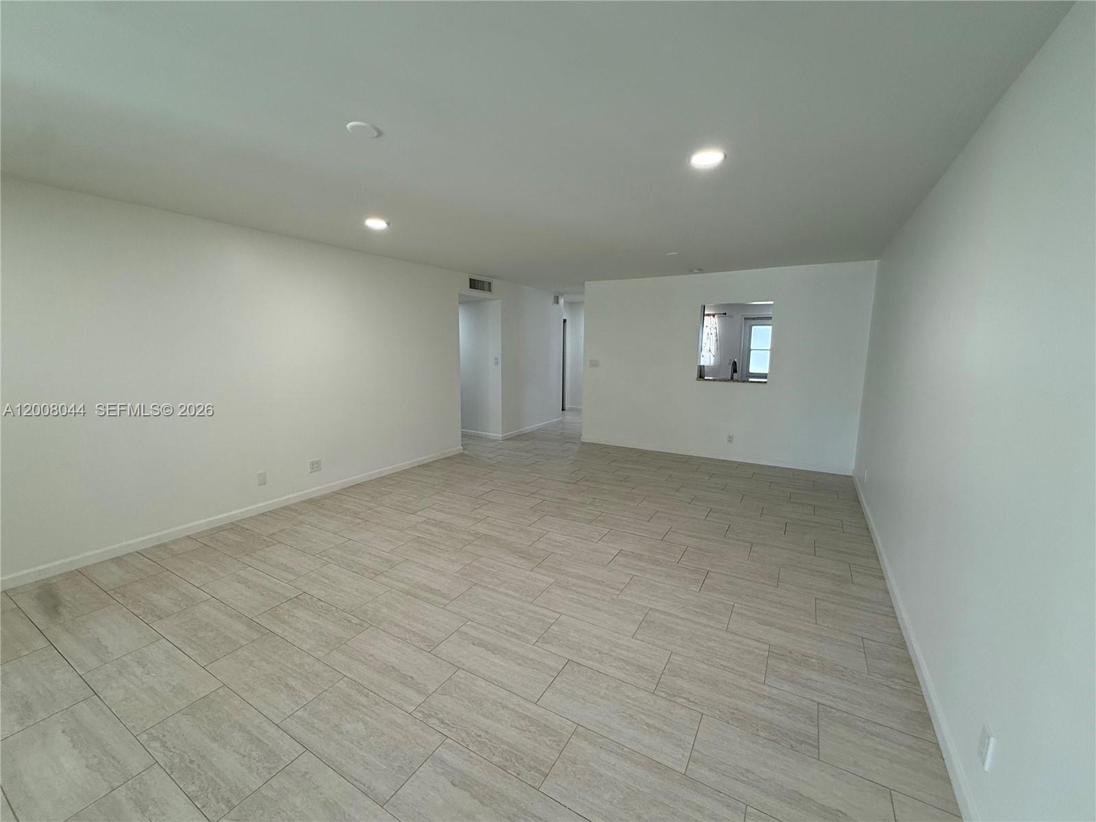 An empty room features light-colored tile flooring, white walls, recessed lighting, and a pass-through window — 609 NE 14th Ave # 108, Hallandale Beach FL 33009, HALLANDALE BEACH, FL