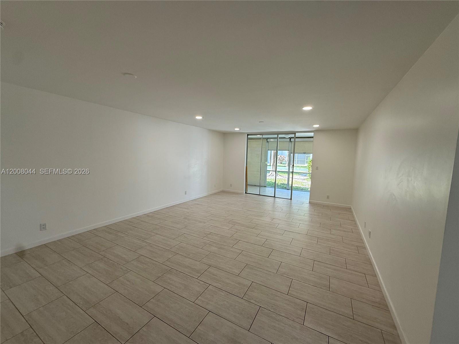 This empty living room features light-colored tile flooring, recessed lighting, and a sliding glass door — 609 NE 14th Ave # 108, Hallandale Beach FL 33009, HALLANDALE BEACH, FL