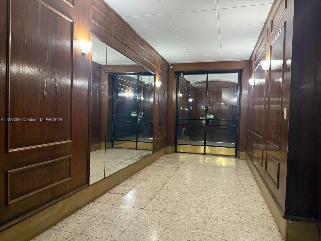 A hallway features wood-paneled walls, a large mirror, and a tiled floor leading to glass doors — 128 Bernardo de Irigoyen Montserrat # 7, FL 128, FL