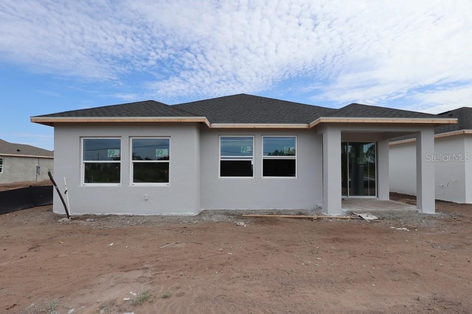 The exterior of a newly constructed single-story house with gray stucco walls and a covered patio — 5027 ORINOCO LANE, ST CLOUD, FL