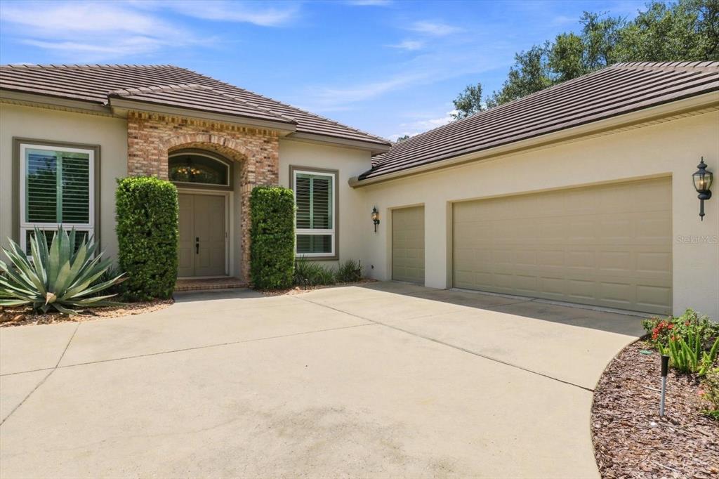 A beige stucco house features a brick-accented entryway, a multi-car garage, and a concrete driveway — 3405 N SPYGLASS VILLAGE PATH, LECANTO, FL
