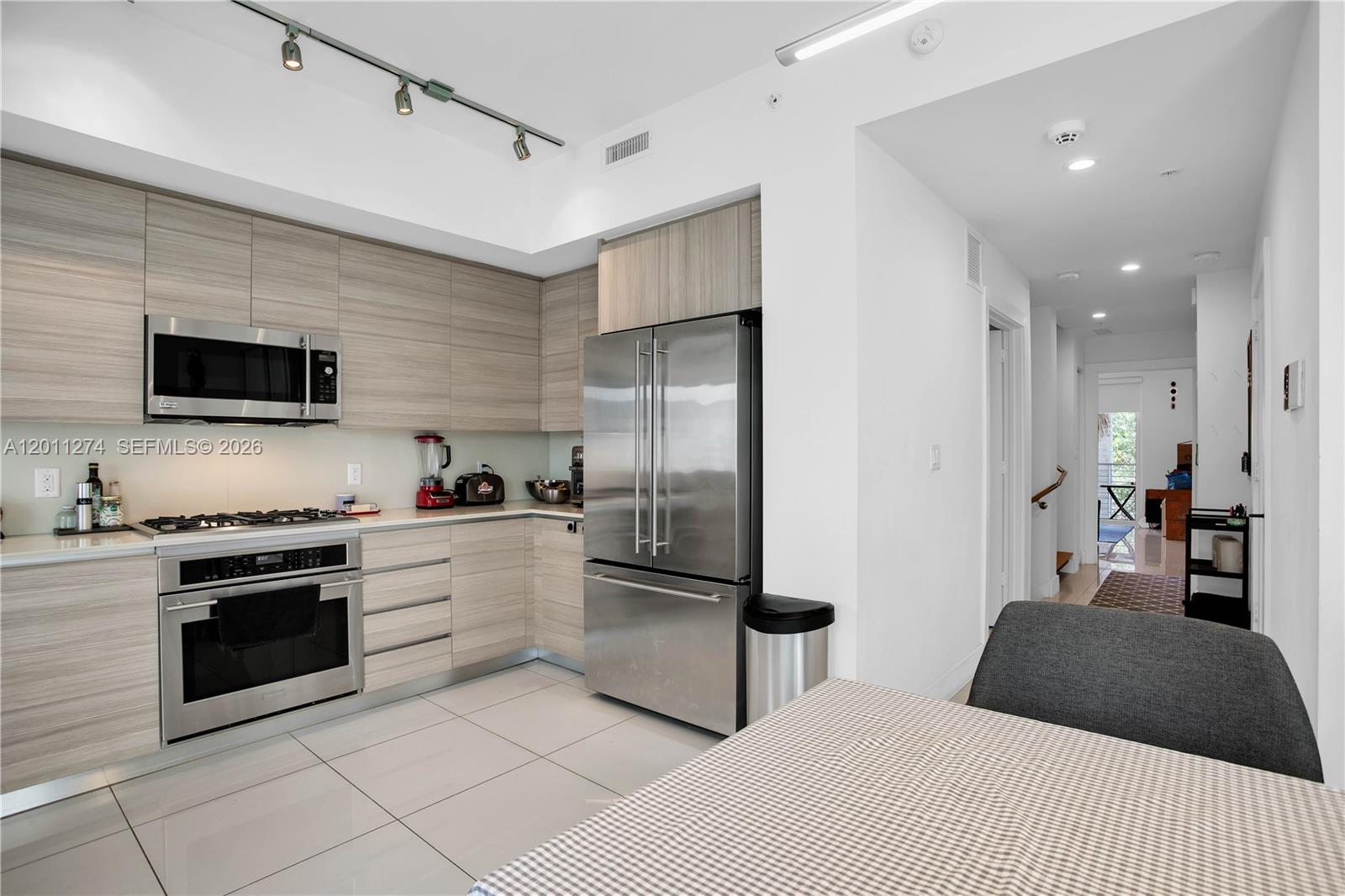 A modern kitchen features light wood cabinetry, stainless steel appliances, and white tile flooring — 87 N Shore Dr, Miami Beach FL 33141, MIAMI BEACH, FL
