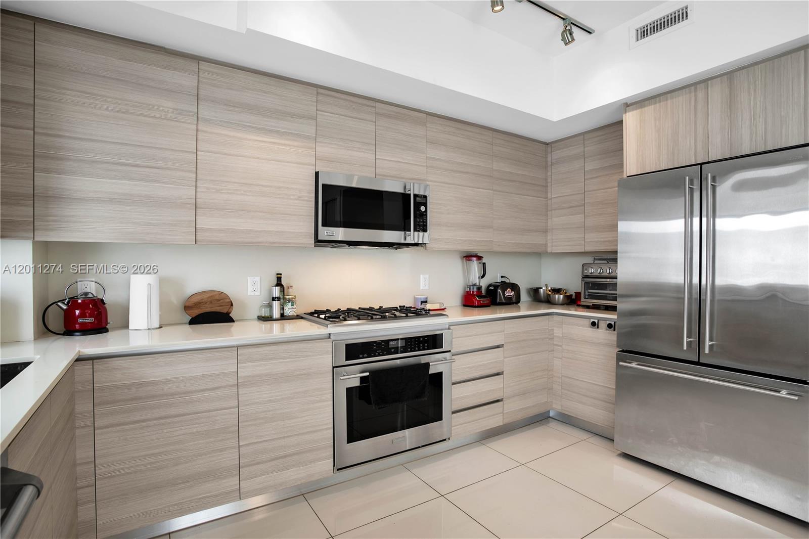 A modern kitchen features light wood-grain cabinetry, stainless steel appliances, and white countertops — 87 N Shore Dr, Miami Beach FL 33141, MIAMI BEACH, FL
