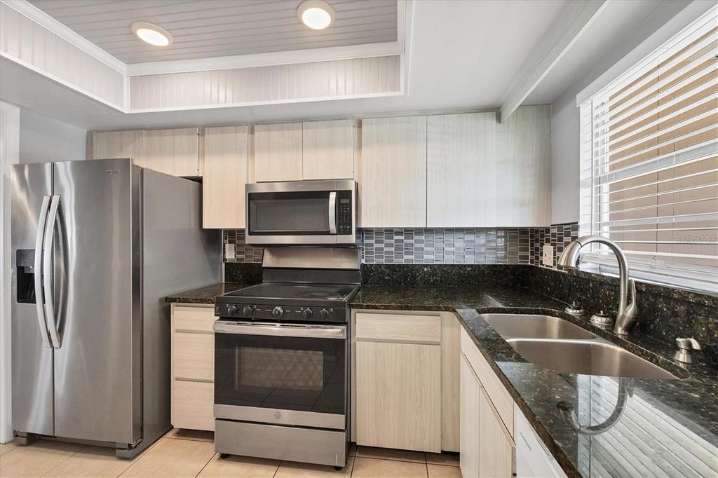 A kitchen features light wood cabinets, dark granite countertops, stainless steel appliances, and tile flooring — 4608 PARK ACRES DRIVE, BRADENTON, FL