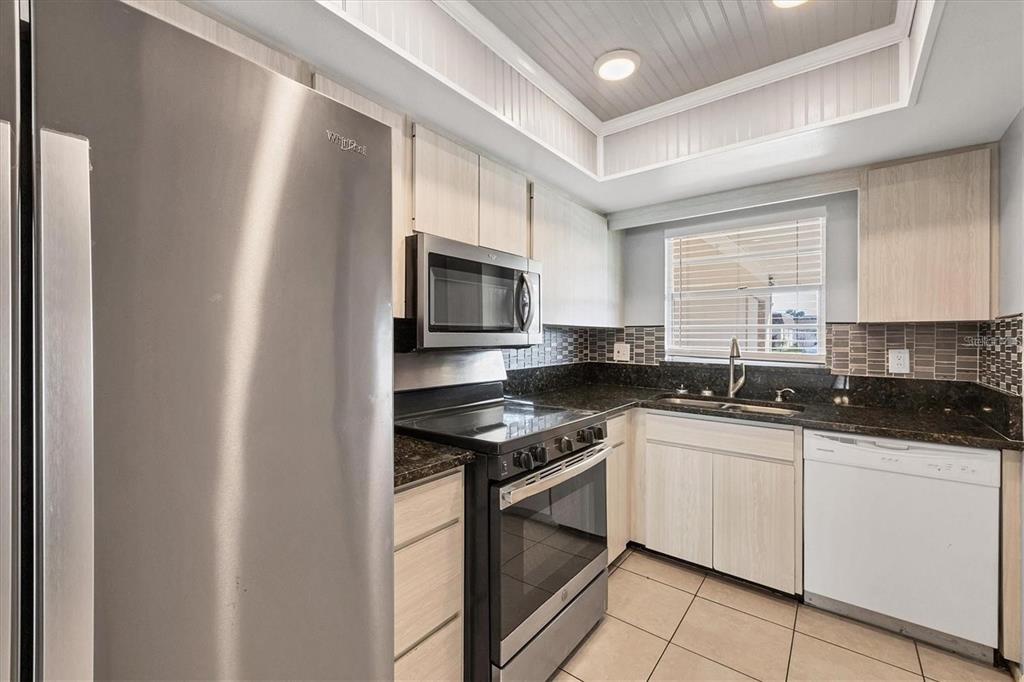 A kitchen features stainless steel appliances, light wood cabinets, dark granite countertops, and tile flooring — 4608 PARK ACRES DRIVE, BRADENTON, FL