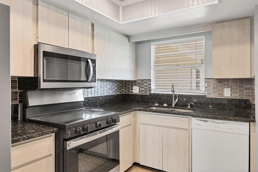 A kitchen features light wood cabinets, dark granite countertops, stainless steel appliances, and a tiled backsplash — 4608 PARK ACRES DRIVE, BRADENTON, FL