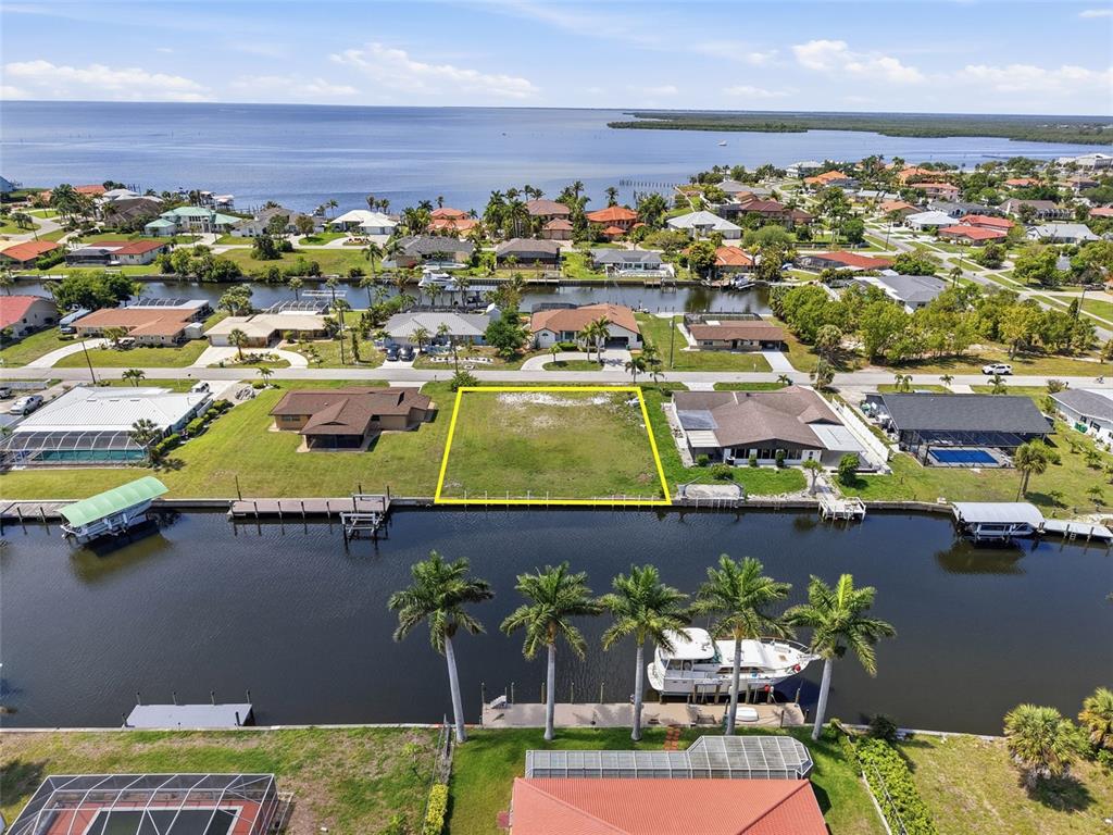 An aerial view shows a vacant waterfront lot highlighted in yellow between two residential homes — 108 SINCLAIR STREET SE, PORT CHARLOTTE, FL
