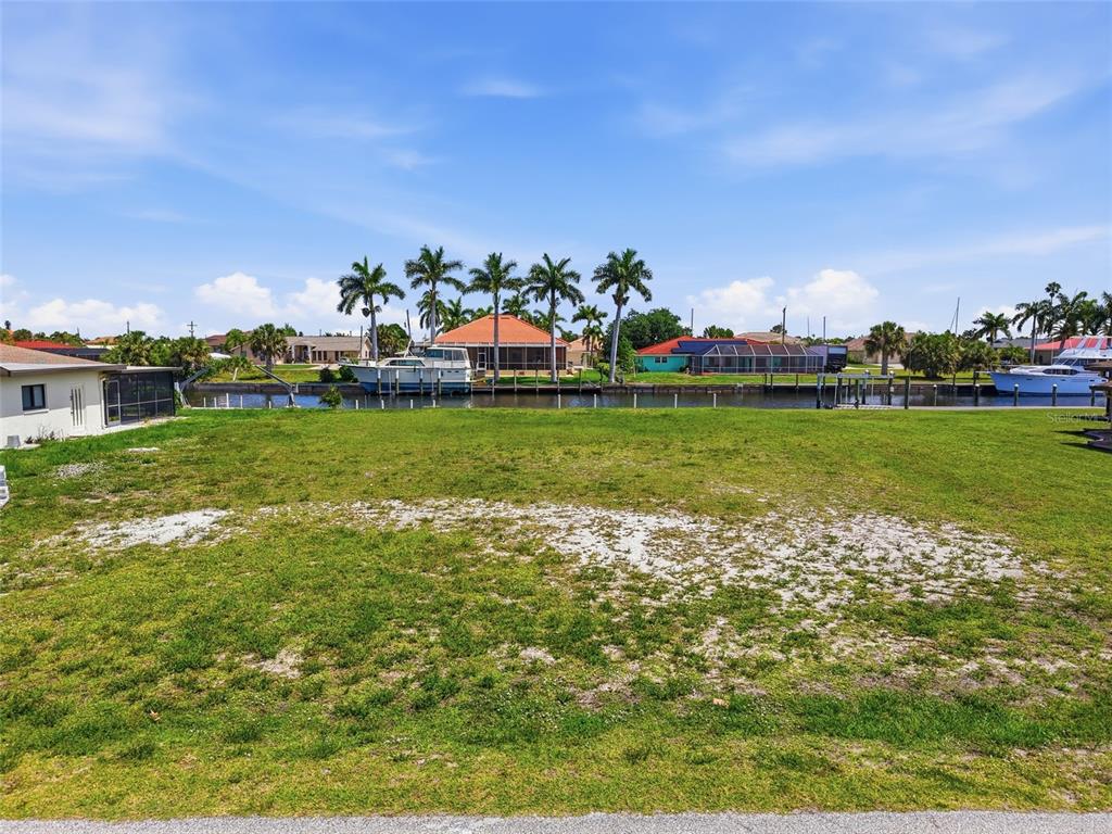 A vacant, grassy waterfront lot features a canal with docked boats and palm trees — 108 SINCLAIR STREET SE, PORT CHARLOTTE, FL