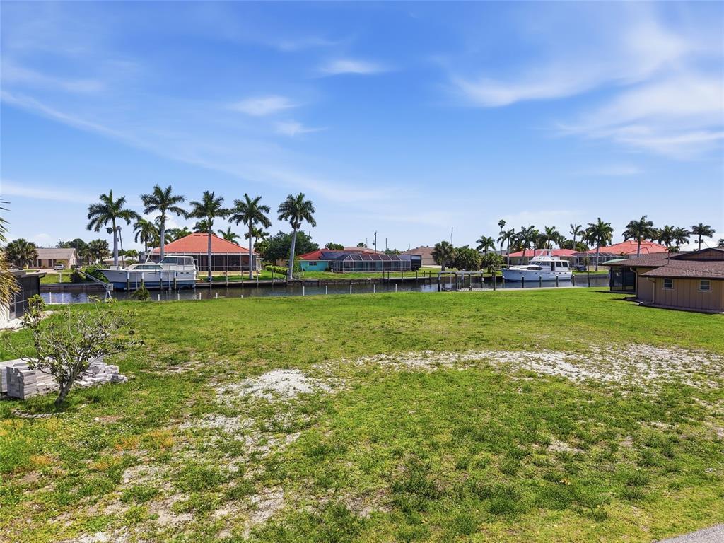 A vacant grassy lot overlooks a canal with docked boats and houses in the background — 108 SINCLAIR STREET SE, PORT CHARLOTTE, FL