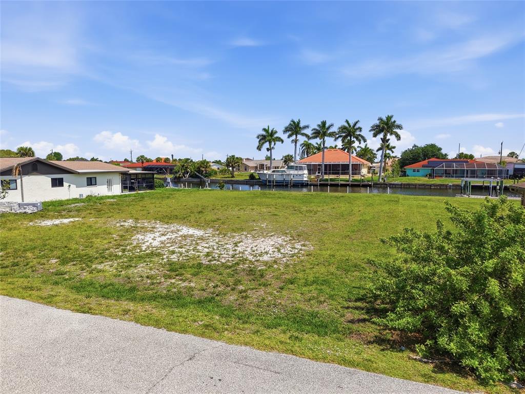 A vacant, grassy waterfront lot sits along a canal with houses and palm trees nearby — 108 SINCLAIR STREET SE, PORT CHARLOTTE, FL