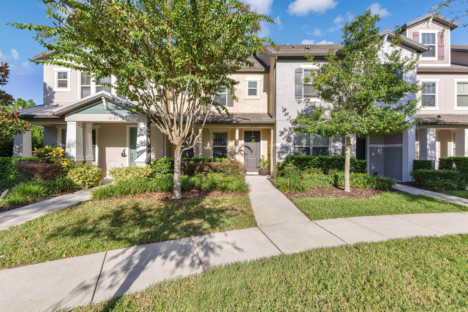 A row of two-story townhomes with beige and gray siding, front porches, and landscaped yards — 5120 Caspian Street, FL 34771, FL