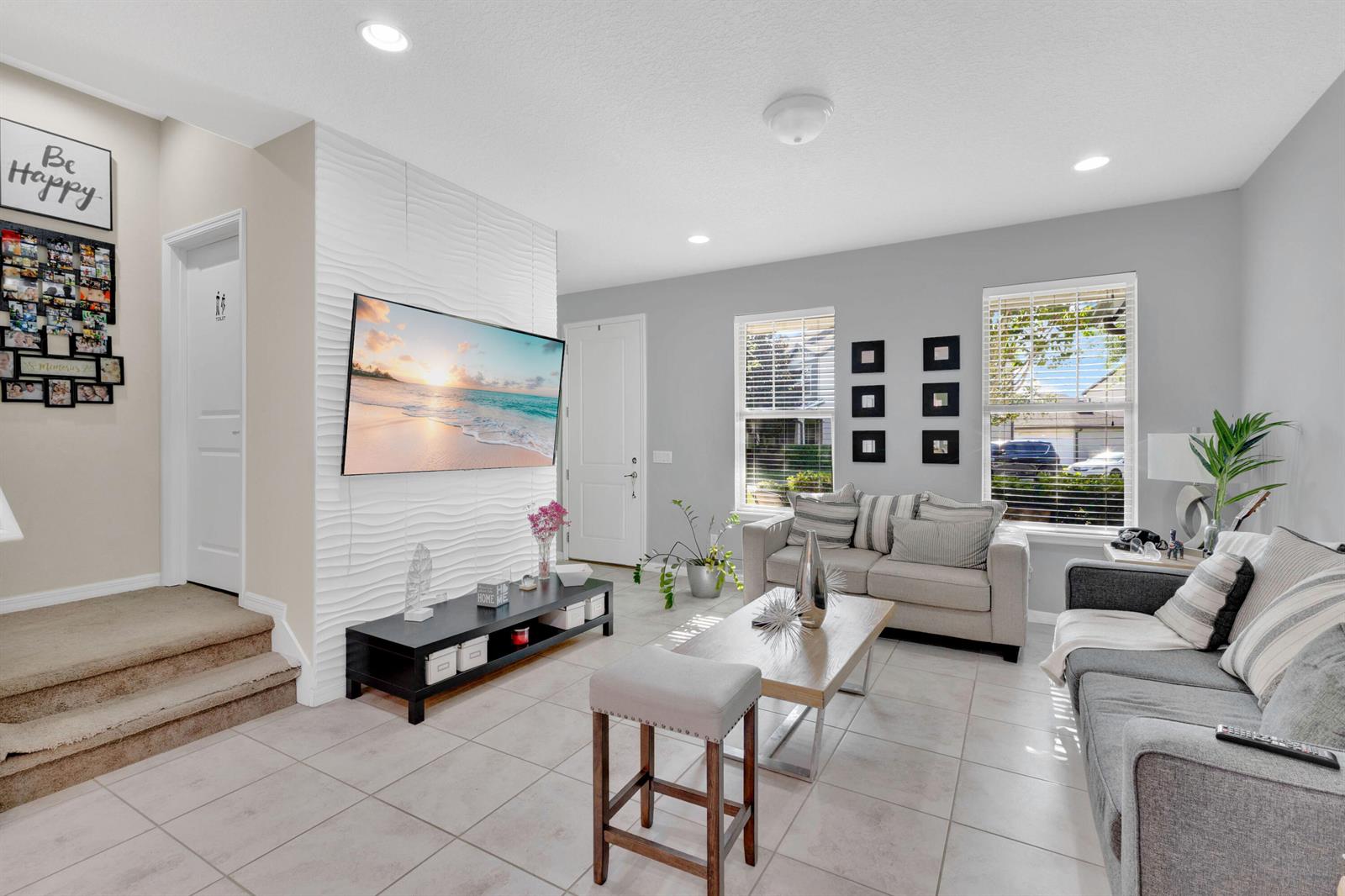 A living room features a textured white accent wall with a mounted television and tile flooring — 5120 Caspian Street, FL 34771, FL