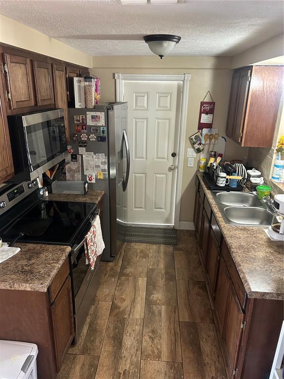 A galley kitchen features wood cabinets, laminate countertops, stainless steel appliances, and wood-look tile flooring — 10824 INGLEWOOD AVENUE, PORT RICHEY, FL