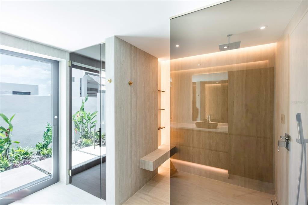 A modern bathroom features wood-look tile, a glass-enclosed shower, and a door to a garden — RESIDENCES AT RIO CALLE EBRO CORNER UNIT 69, BAYAMON, PR