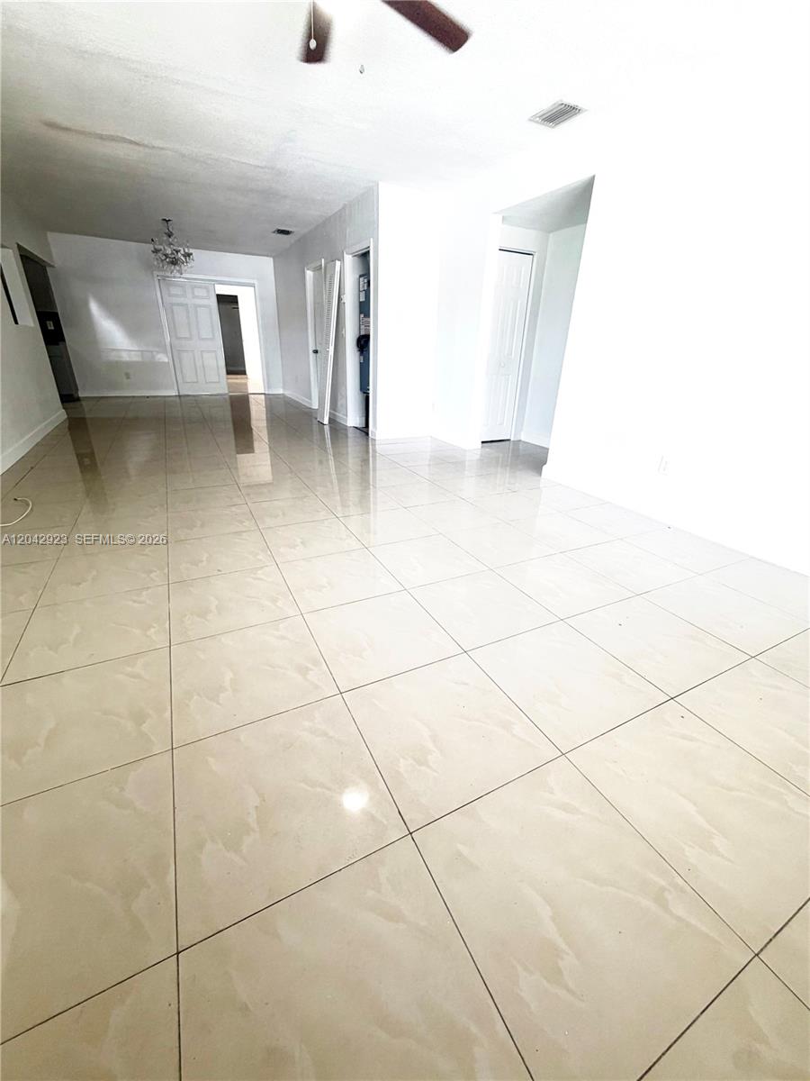 An empty room features light-colored tile flooring, white walls, and a ceiling fan — MIAMI, FL
