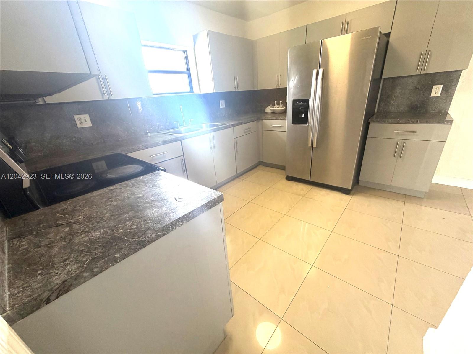 A kitchen features light gray cabinets, dark stone countertops, stainless steel appliances, and tile flooring — MIAMI, FL