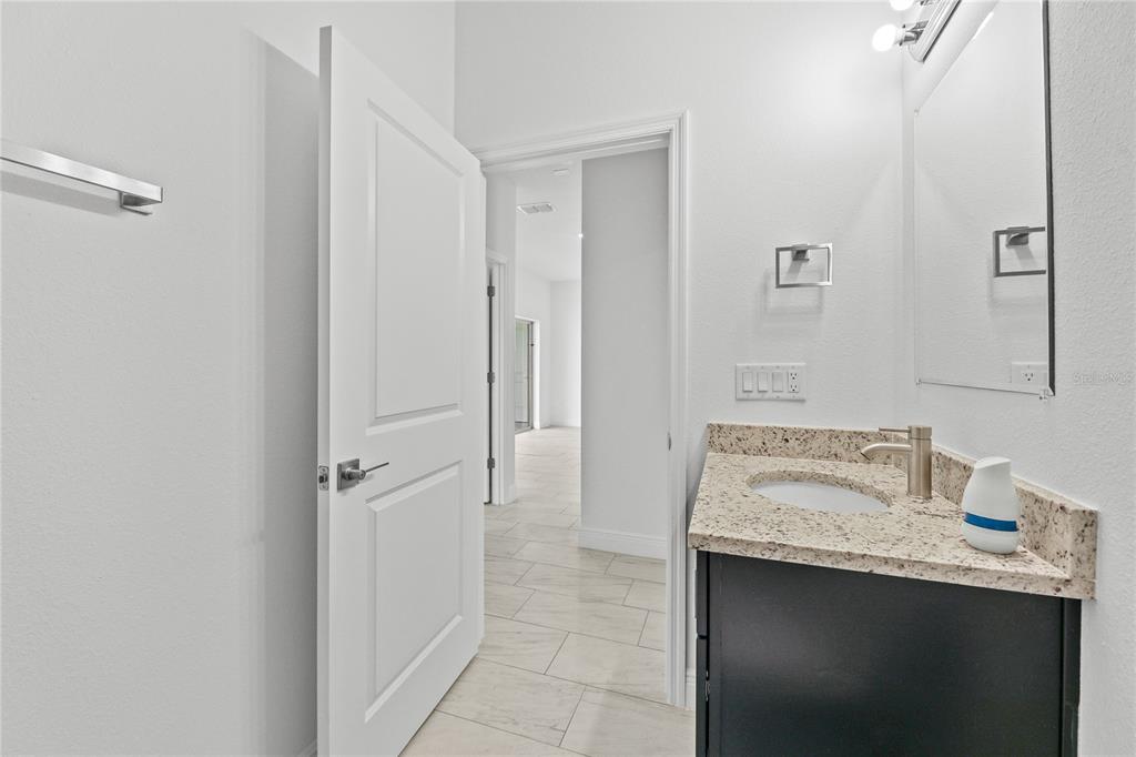 A bathroom features a dark vanity with a granite countertop, a mirror, and a doorway — 8539 SW 129TH LANE, OCALA, FL
