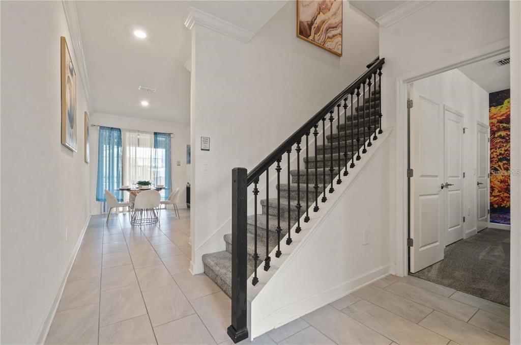 An interior view shows a tiled entryway with a staircase featuring black railings and carpet — 4363 SCENE LN, KISSIMMEE, FL