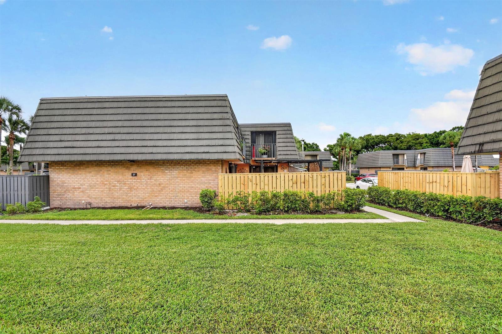 A brick townhouse exterior features a mansard roof, a wooden privacy fence, and green landscaping — 315 3rd Way, West Palm Beach FL 33407, WEST PALM BEACH, FL