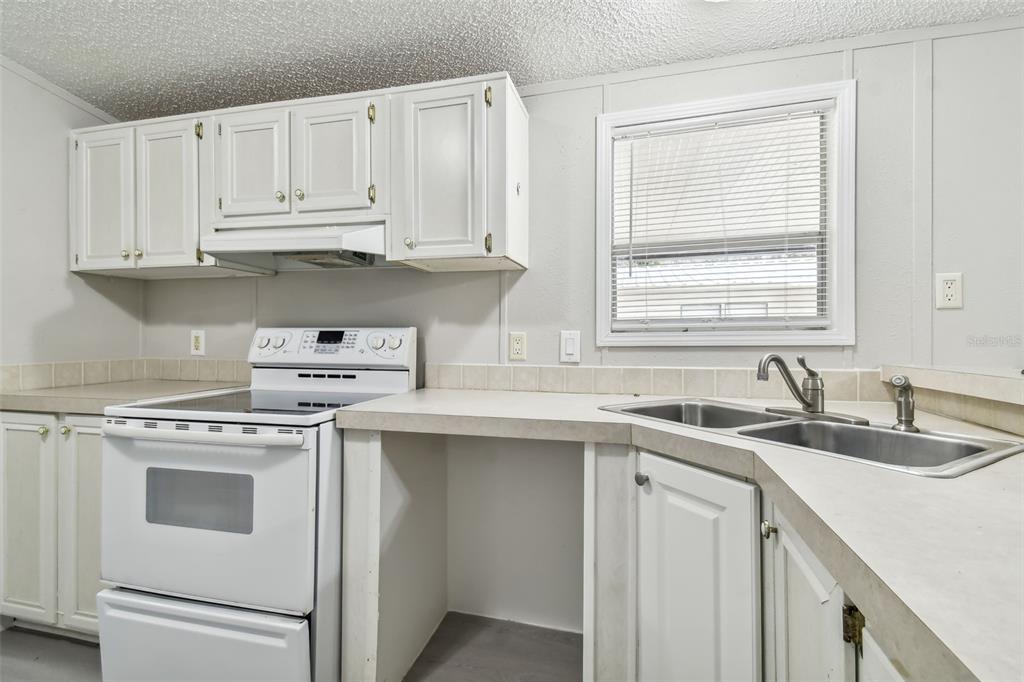 A kitchen features white cabinets, a white stove, a double sink, and a window — 10607 BAY HILLS CIRCLE, THONOTOSASSA, FL