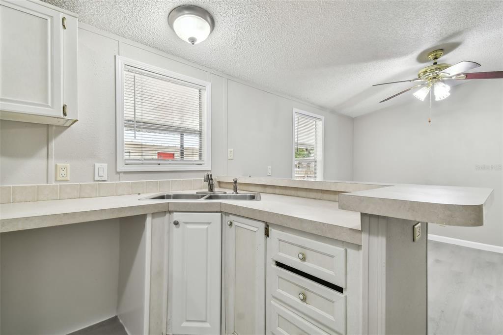 A kitchen features white cabinets, a corner sink, and a breakfast bar overlooking a room — 10607 BAY HILLS CIRCLE, THONOTOSASSA, FL