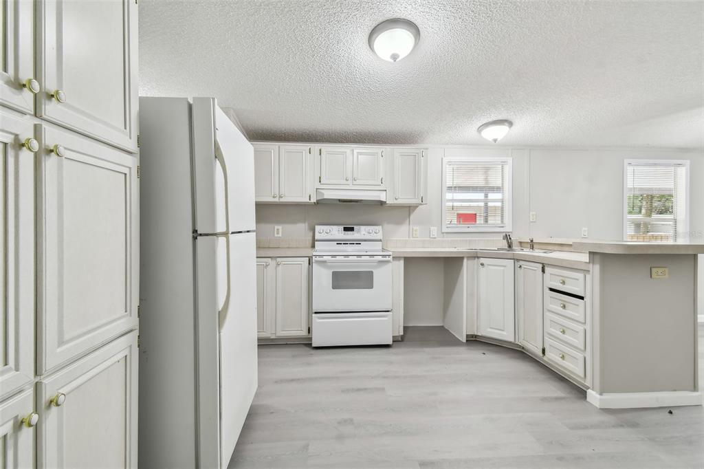 A kitchen with white cabinets, white appliances, and light-colored wood-look flooring — 10607 BAY HILLS CIRCLE, THONOTOSASSA, FL