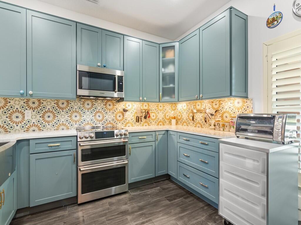A kitchen features blue cabinets, stainless steel appliances, and a patterned yellow and white backsplash — 1643 Baseline Lane, Vero Beach FL 32967, VERO BEACH, FL