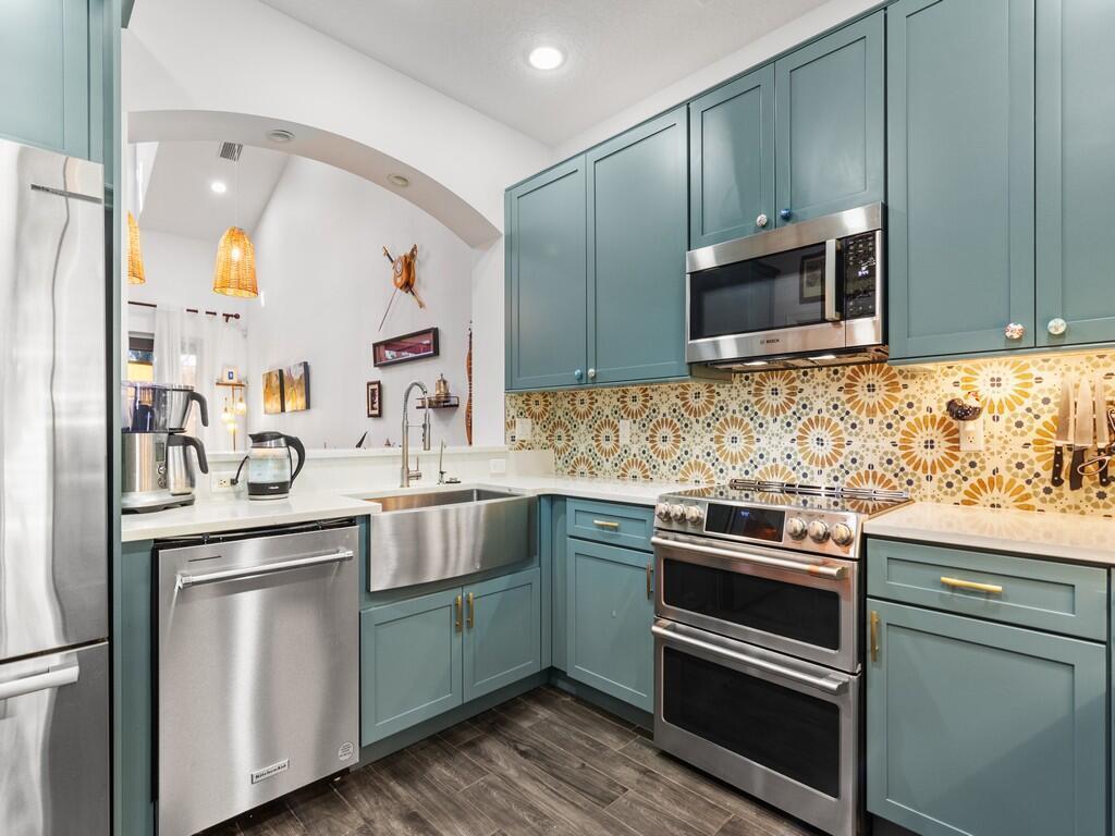 A kitchen features teal cabinets, a stainless steel farmhouse sink, and a patterned tile backsplash — 1643 Baseline Lane, Vero Beach FL 32967, VERO BEACH, FL