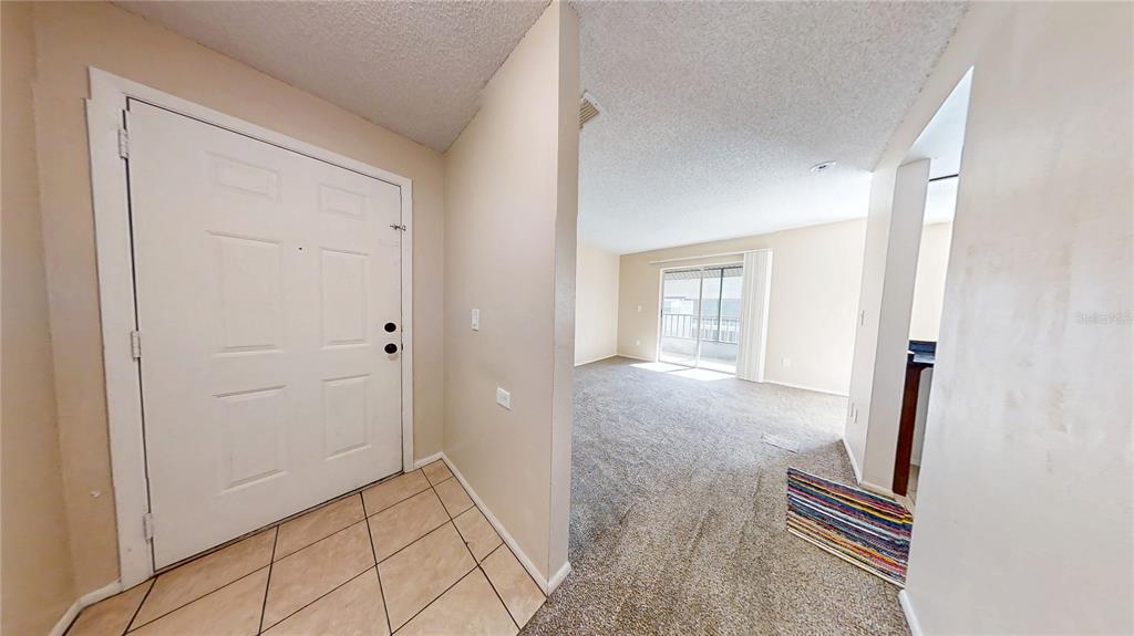 An entryway with tiled flooring leads into a carpeted living area with a sliding glass door — 417 BANANA CAY DRIVE UNIT J, SOUTH DAYTONA, FL